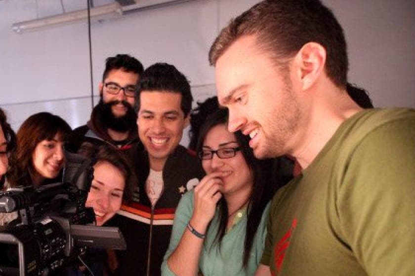 Kryshan Randel laughing with a group of students as they look at the screen of a video camera.