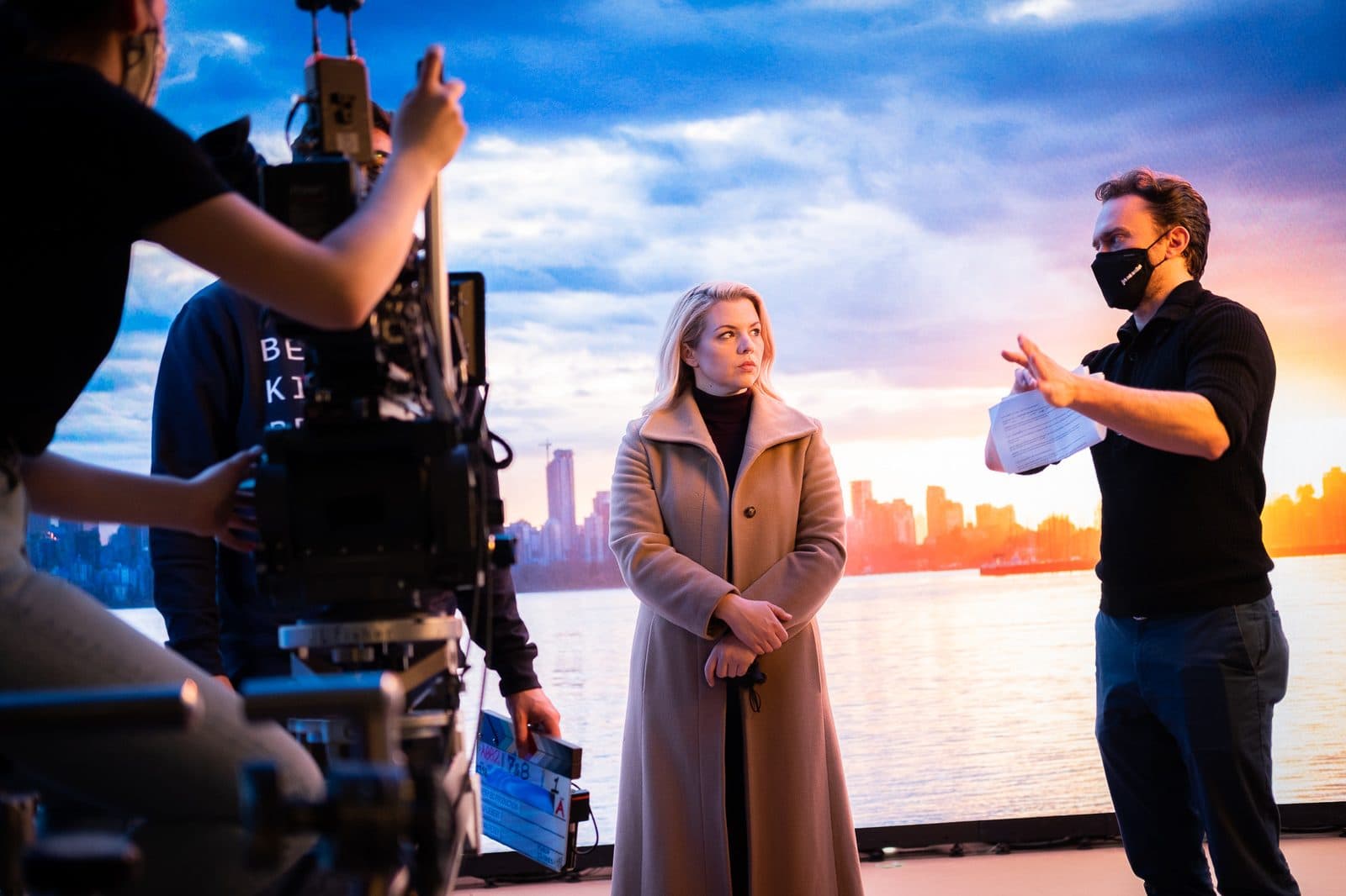 Kryshan Randel, masked, directing an actor on an LED-wall stage, with a camera crew in the foreground.